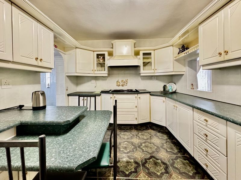 A functional kitchen featuring white cabinetry, a built-in hob with extractor fan, and a green laminate countertop with an integrated breakfast bar.
