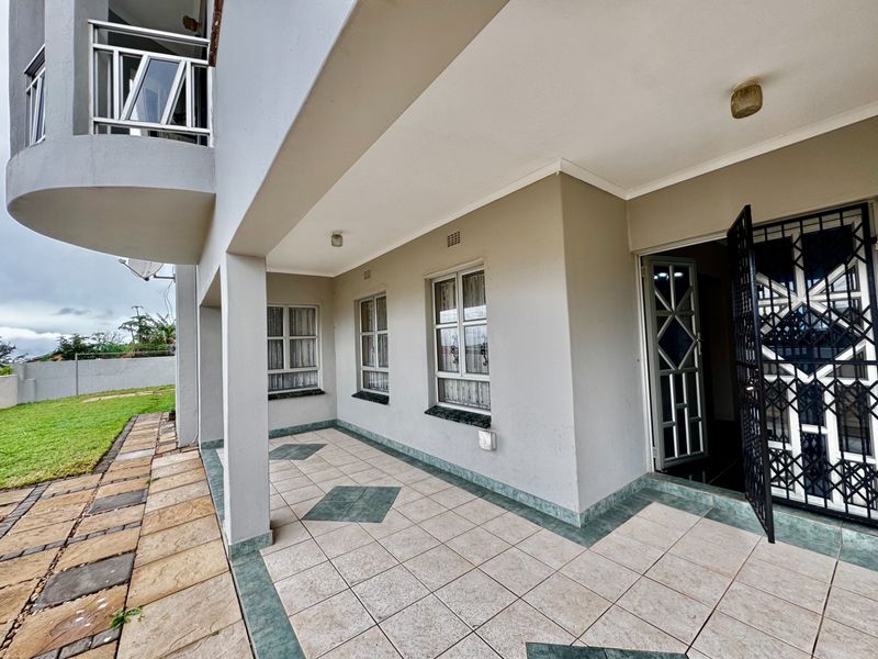 A covered patio area featuring tiled flooring, security gates, and access to the garden, providing a functional outdoor living space.