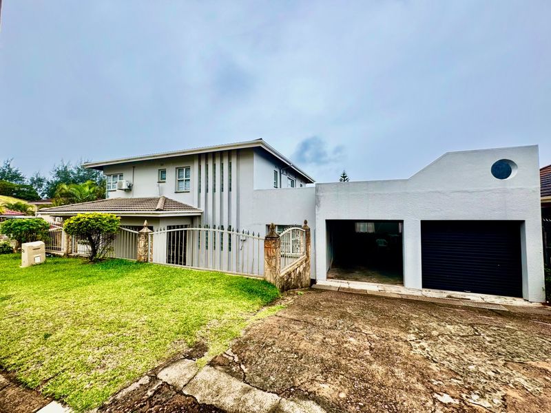 A two-story residential property featuring a double garage, paved driveway, and front garden with metal perimeter fencing.