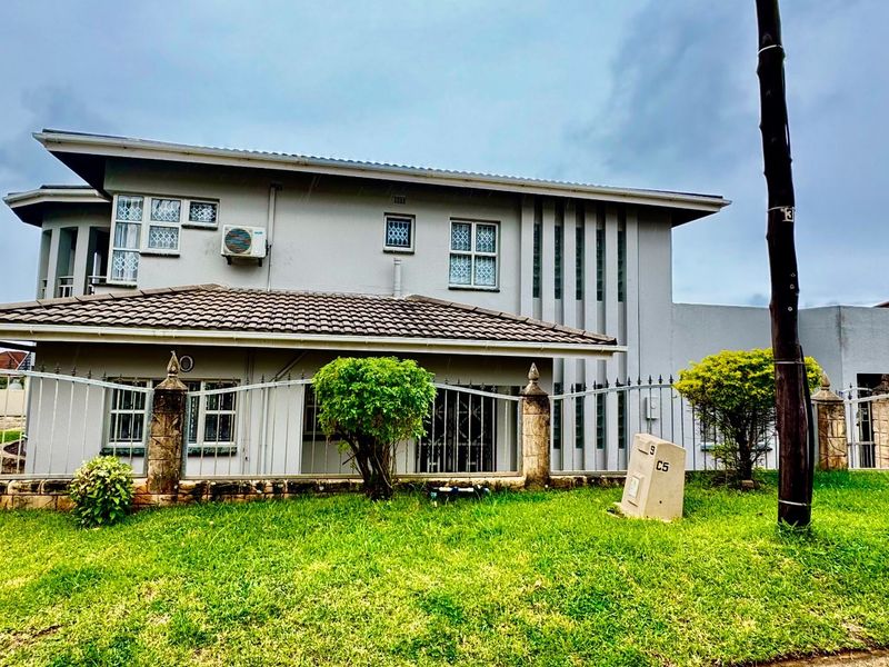A two-story residential property featuring a tiled roof, exterior wall-mounted air conditioning unit, and perimeter metal fencing with stone pillars.