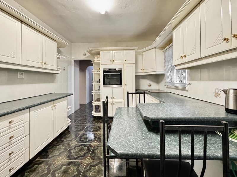 A functional kitchen featuring white cabinetry, integrated oven, and a breakfast bar with laminate countertops and patterned floor tiles.