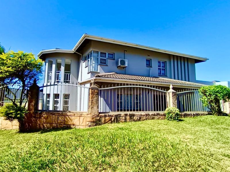 A two-story residential property featuring a stone-clad boundary wall, metal fencing, and a well-maintained lawn in the front garden area.
