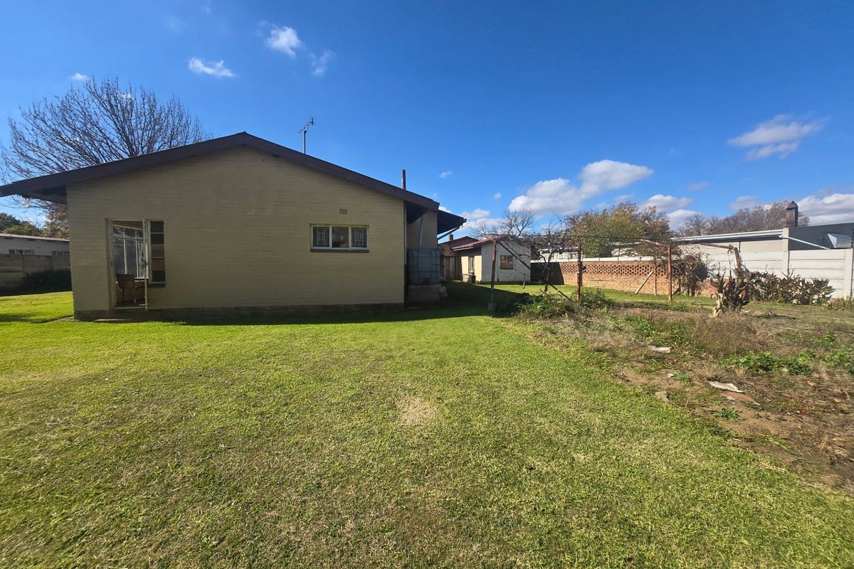 Rear view of the property featuring a large lawn, brick boundary wall, and established garden space with a water tank.