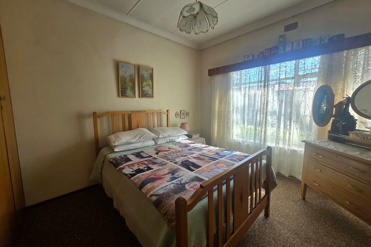 A standard bedroom featuring a large window, built-in wardrobe, and classic ceiling cornice, offering a functional space with potential for modernization.