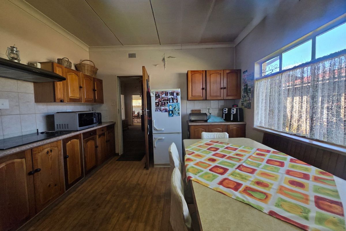 A dated kitchen featuring wooden cabinetry, laminate countertops, and a large window, showing signs of wear and ceiling damage.