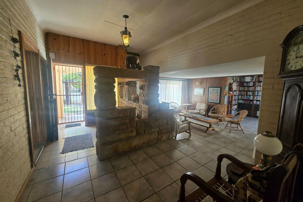 Spacious living area featuring a prominent stone fireplace, tiled flooring, timber wall accents, and built-in shelving, offering a rustic and character-filled interior space.
