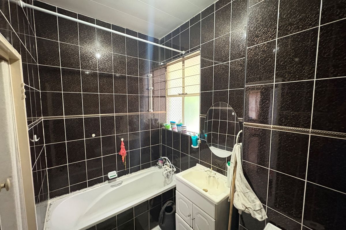 A compact bathroom featuring dark wall tiles, a built-in bathtub, a vanity basin, and a window for natural light.