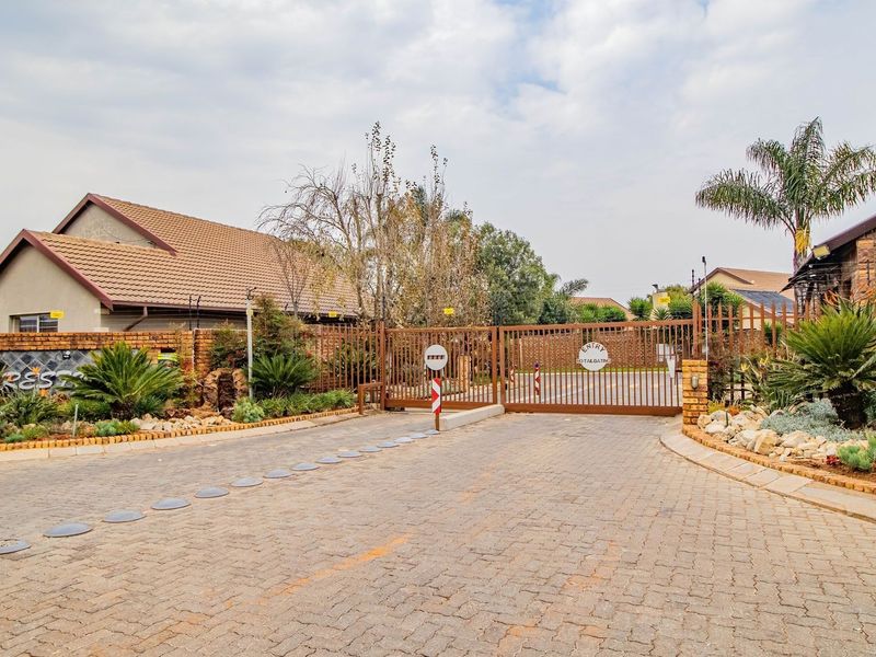 A secure gated entrance to a residential estate featuring paved driveway access, brick boundary walls, and established landscaped gardens.
