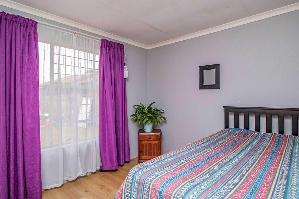 A functional bedroom featuring laminate flooring, a large window with security bars, and neutral wall finishes.