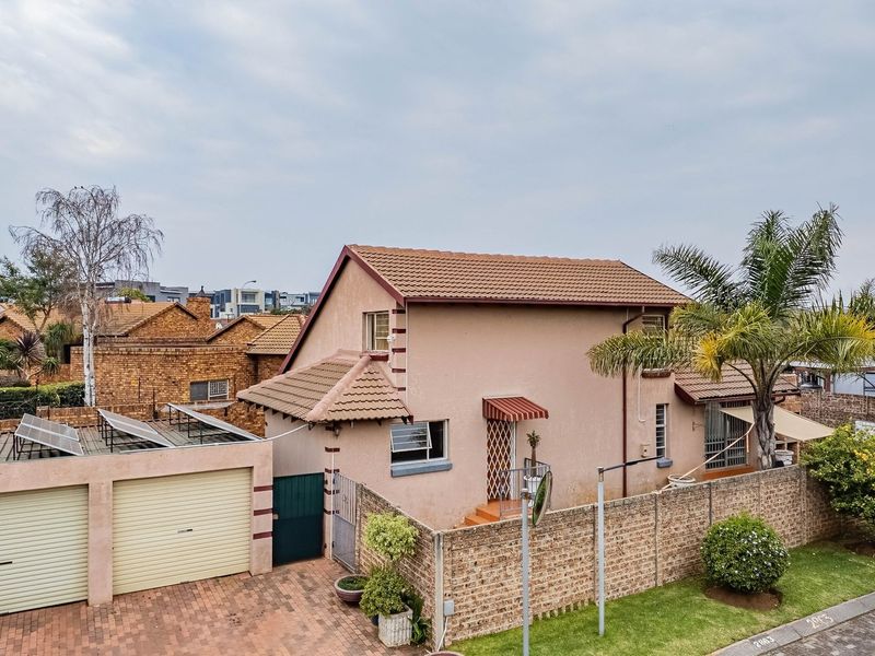 An elevated view of a residential property featuring a double garage with solar panels, a paved driveway, and a secure brick boundary wall.