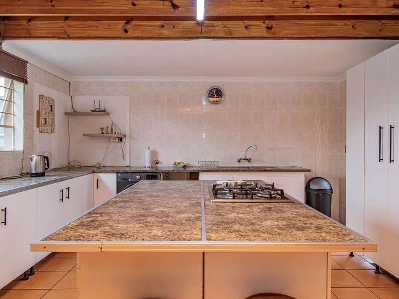 A functional kitchen featuring exposed timber ceiling beams, a central island with a built-in gas hob, tiled backsplash, and ample built-in cabinetry.