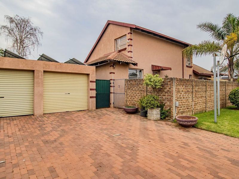 Front exterior view of a residential property featuring a double garage with roller shutter doors, a paved driveway, and a brick boundary wall.