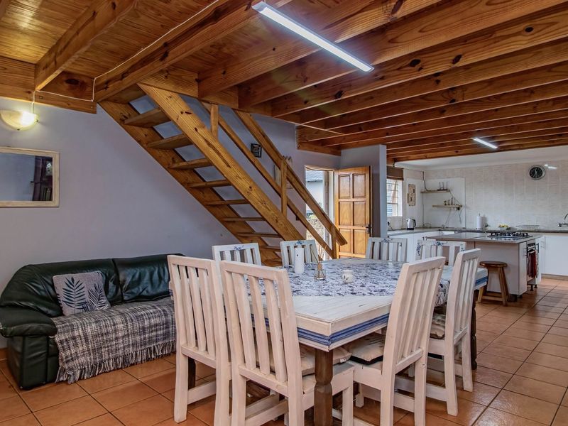 Open-plan living and dining area featuring exposed timber ceiling beams, a wooden staircase, and an adjoining kitchen with tiled flooring throughout.