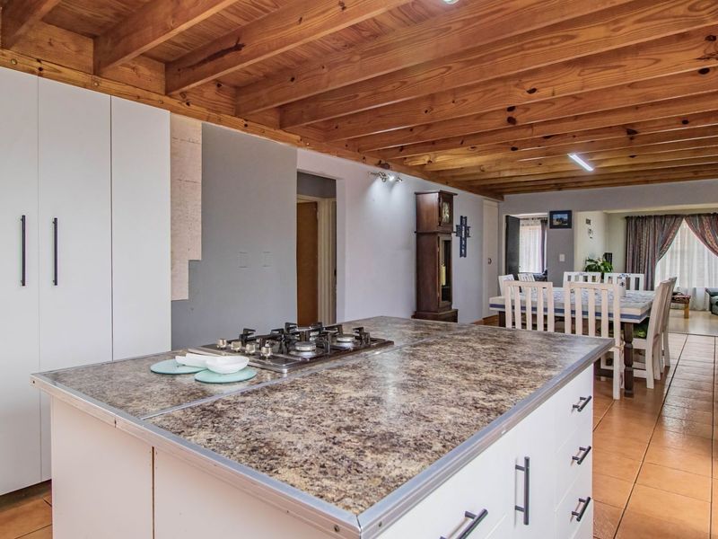 Open plan living area featuring a kitchen island with gas hob, exposed timber beam ceilings, and tiled flooring throughout.