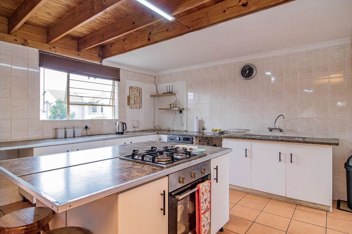 Functional kitchen featuring a central island with a gas hob, built-in oven, exposed timber ceiling beams, and ample tiled workspace.