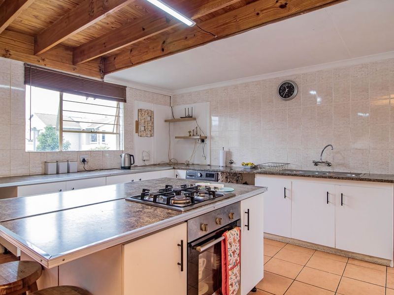 Functional kitchen featuring a central island with a gas hob, built-in oven, exposed timber ceiling beams, and ample tiled workspace.