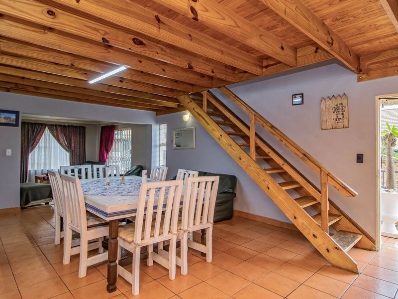 Open plan living and dining area featuring exposed timber ceiling beams, tiled flooring, and a wooden staircase leading to the upper level.