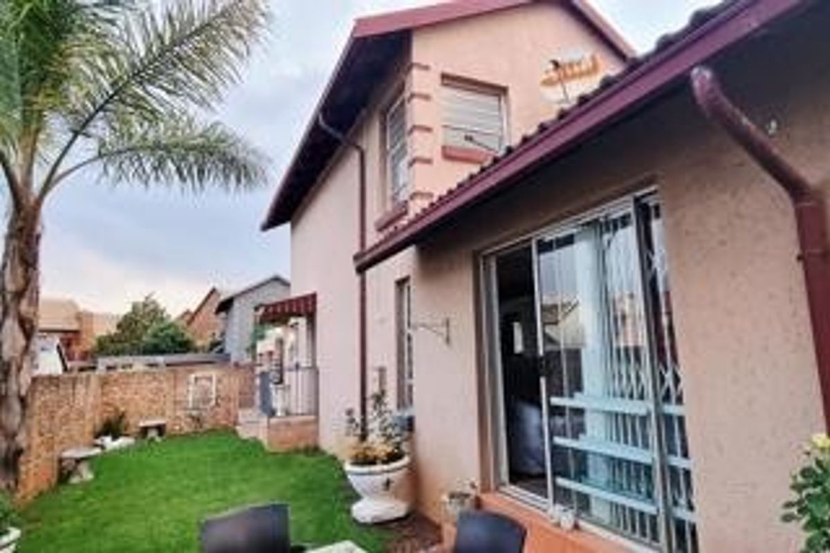 Rear view of the property featuring a small garden, brick boundary wall, and sliding glass door with security gate access.
