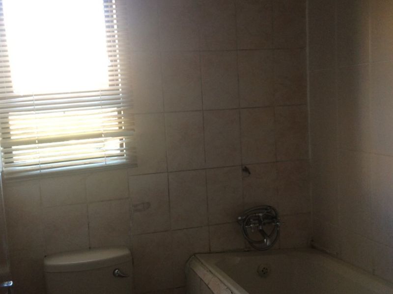 A dated bathroom featuring a bathtub, shower head, and toilet with tiled walls, requiring renovation to update the finishes and fixtures.