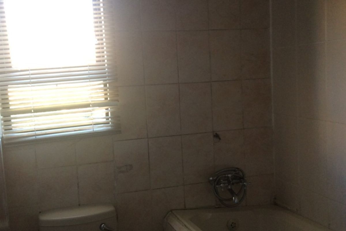 A dated bathroom featuring a bathtub, shower head, and toilet with tiled walls, requiring renovation to update the finishes and fixtures.
