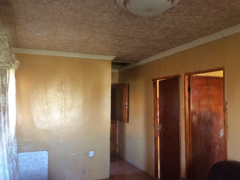 A dated hallway featuring textured ceiling tiles, wooden doors, and worn wall finishes, requiring cosmetic updates and repairs to improve the overall condition.
