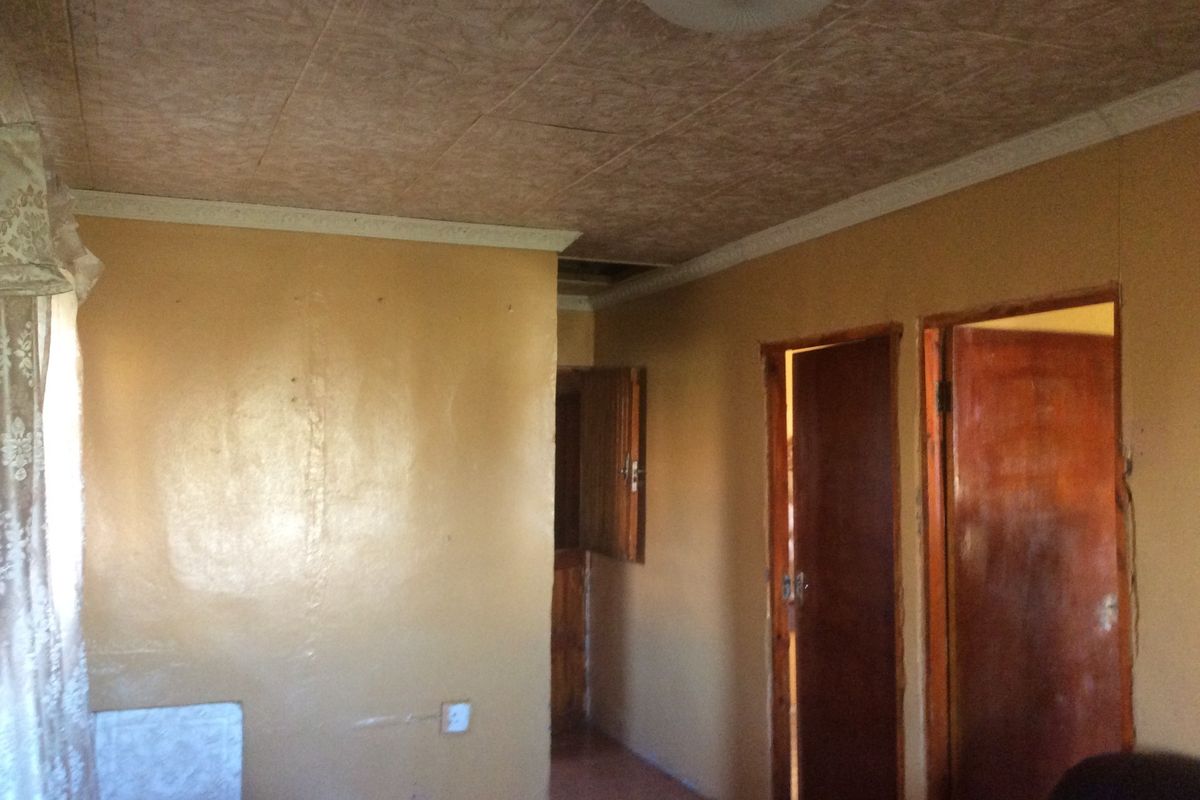 A dated hallway featuring textured ceiling tiles, wooden doors, and worn wall finishes, requiring cosmetic updates and repairs to improve the overall condition.