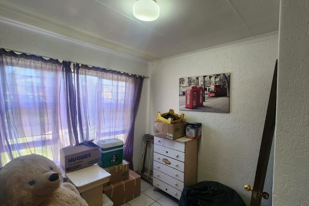 A bedroom featuring tiled flooring and a window with security bars, currently used for storage.