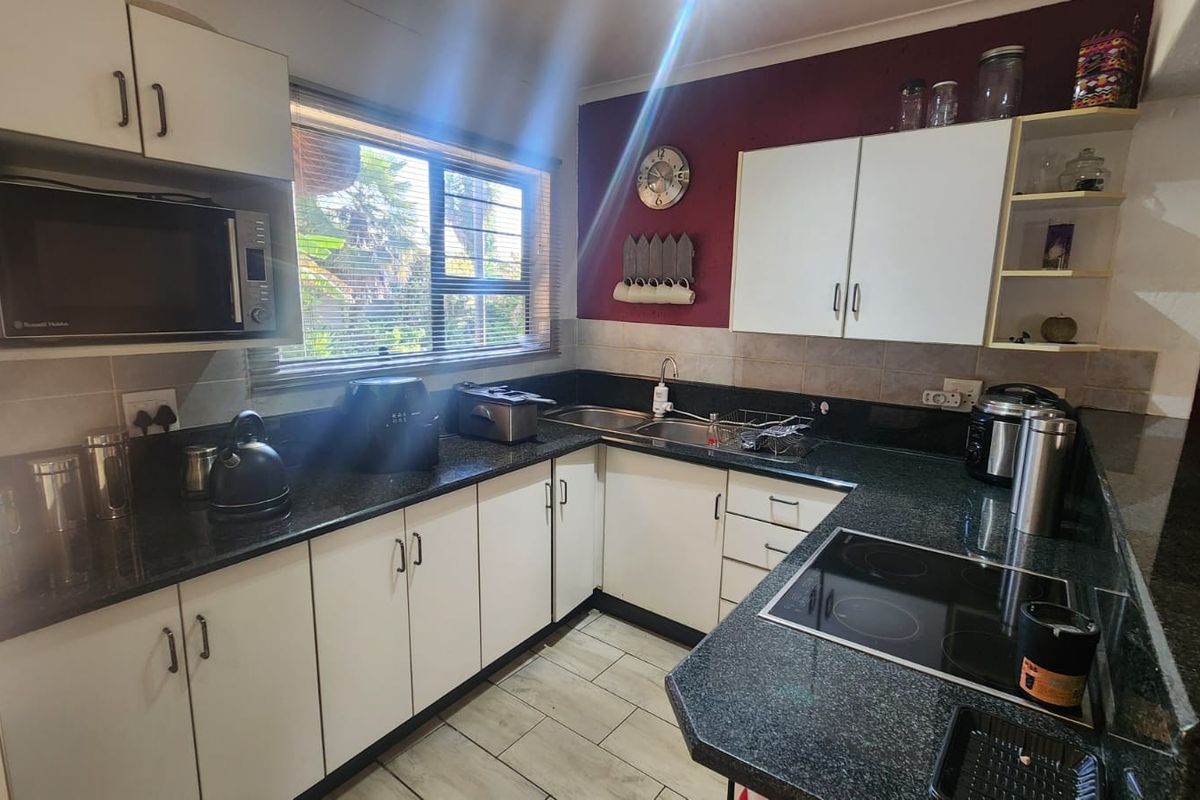 A functional kitchen featuring dark granite countertops, white cabinetry, an integrated electric hob, and a built-in microwave with tiled flooring.