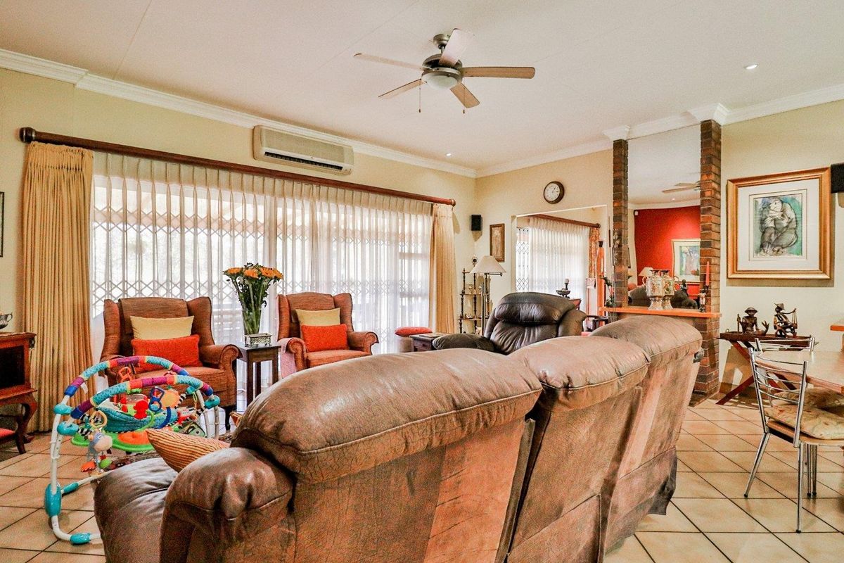 Spacious living area featuring tiled flooring, a ceiling fan, wall-mounted air conditioning unit, and a decorative brick pillar accent.