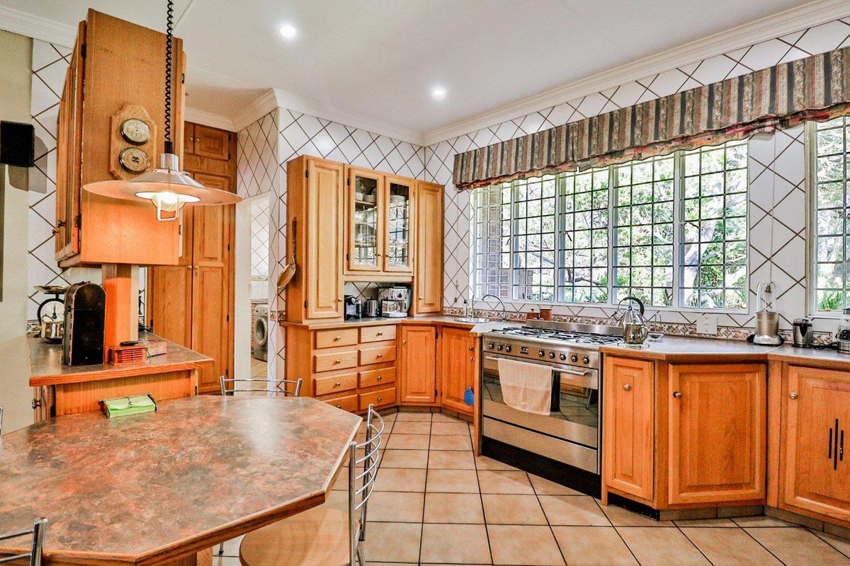 A traditional kitchen featuring wooden cabinetry, a gas stove, tiled flooring, and a large window overlooking the garden.