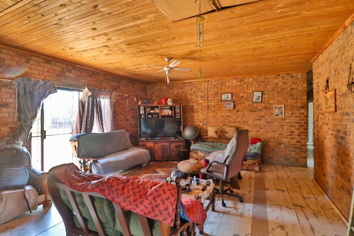 A rustic living room featuring exposed face-brick walls, a timber-clad ceiling, and tiled flooring with direct access to the exterior.