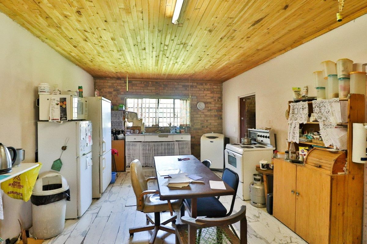 A rustic kitchen area featuring exposed brick walls, a timber-clad ceiling, and basic built-in cabinetry with a functional stove and sink area.