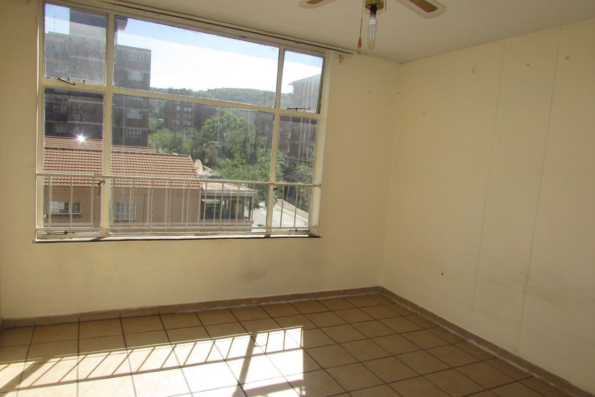 An empty bedroom featuring large windows with urban views, tiled flooring, and a ceiling fan, offering a blank canvas for renovation.