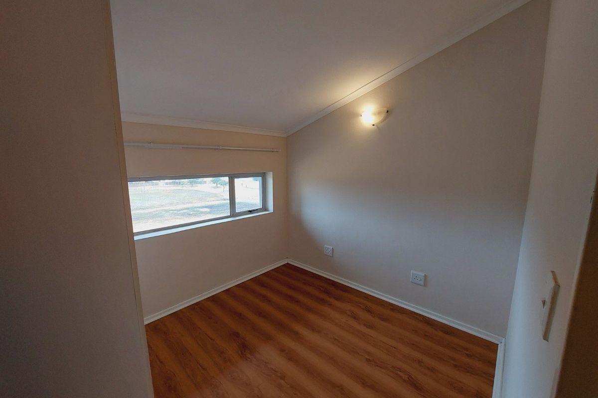 A bright, empty bedroom featuring laminate flooring, a sloped ceiling, and a horizontal window providing natural light.