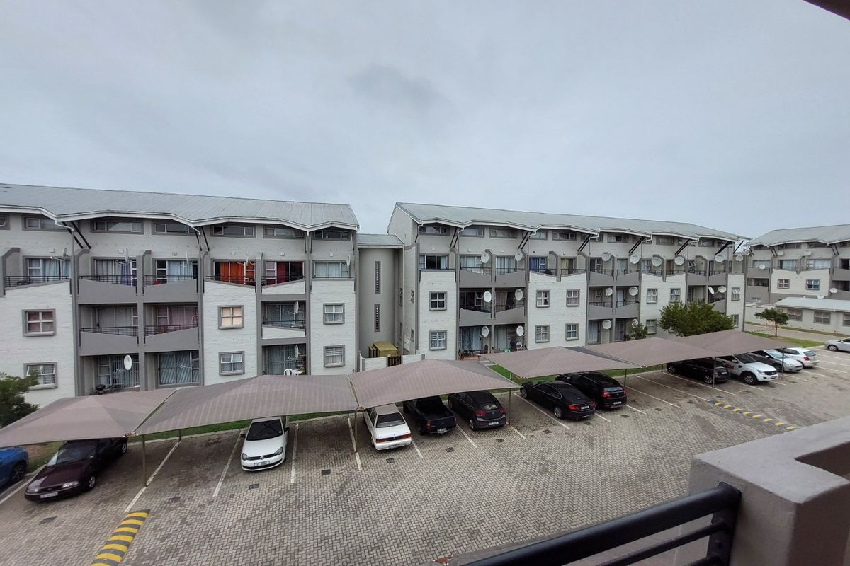 View of the apartment complex exterior, featuring a paved parking area with shade cloth carports and multi-story residential building facades.