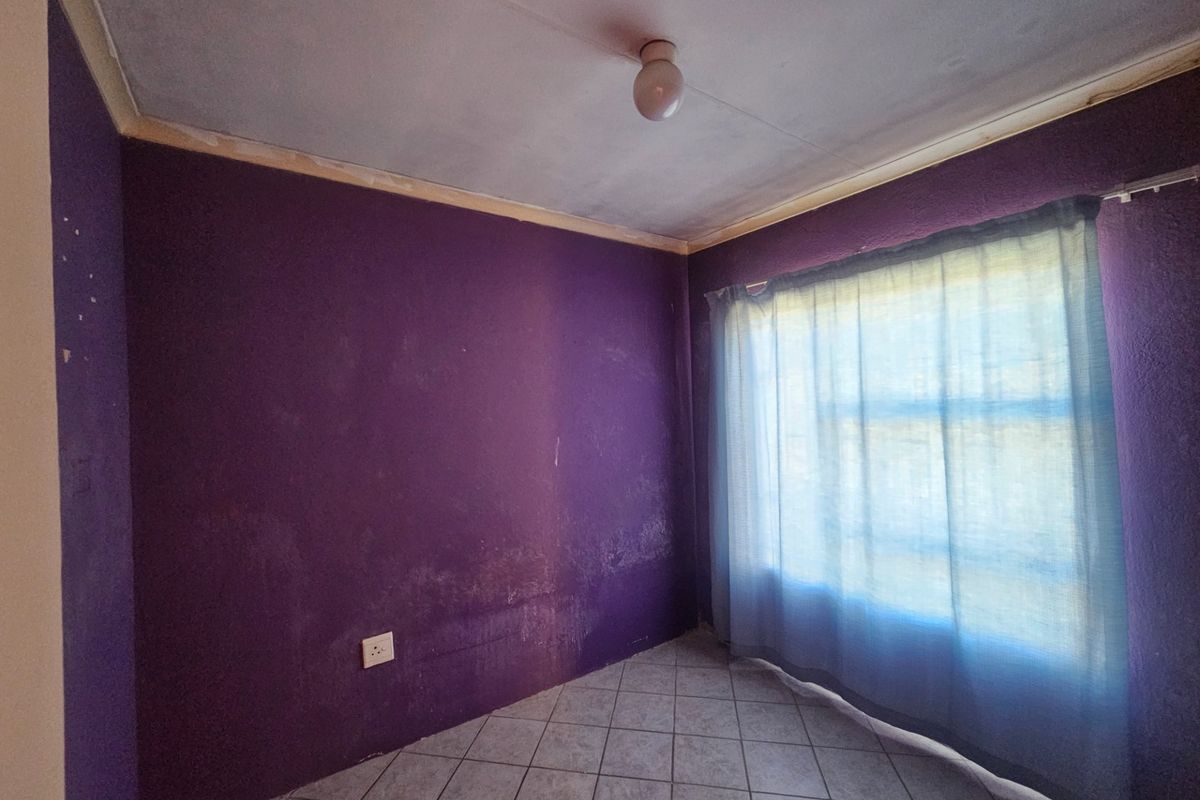 An empty bedroom featuring tiled flooring and a ceiling light fixture, requiring cosmetic updates to the wall finishes.