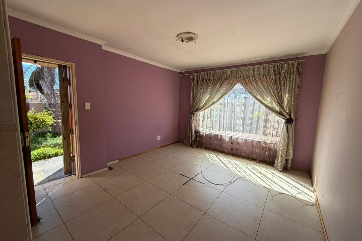 An empty living room featuring tiled flooring, large window with curtains, and direct access to the outdoor garden area.