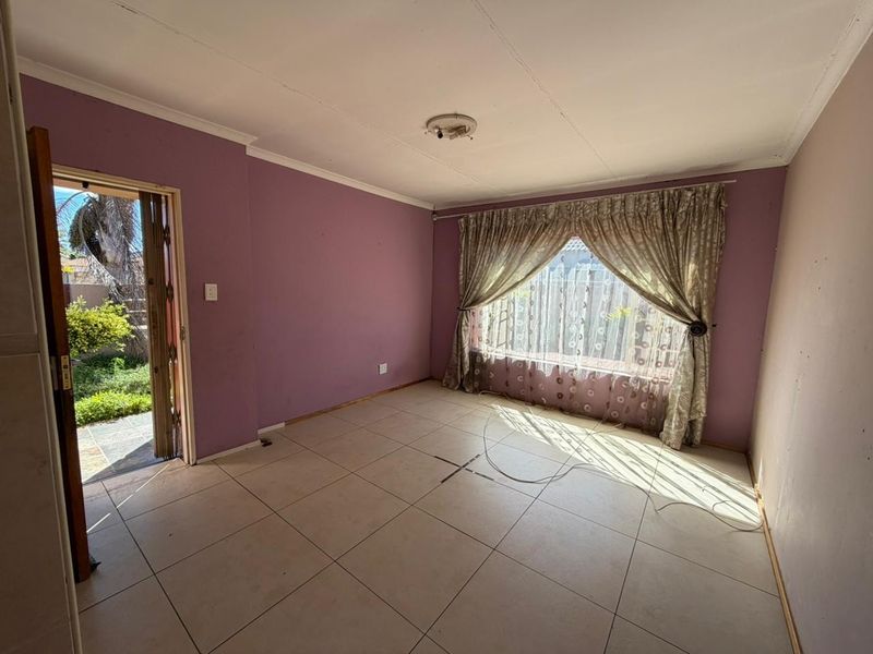 An empty living room featuring tiled flooring, large window with curtains, and direct access to the outdoor garden area.