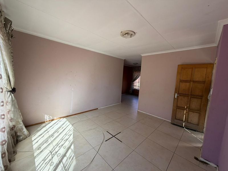 A vacant living area featuring tiled flooring, a wooden panel door, and access to an adjoining room.
