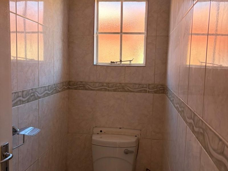 A compact guest toilet featuring floor-to-ceiling ceramic wall tiles, a window for natural light, and a standard porcelain toilet suite.