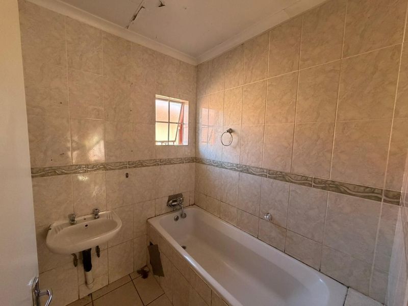 A dated bathroom featuring a standard bathtub, wall-mounted basin, and full-height wall tiling, requiring cosmetic updates and repairs to the ceiling and bathtub panel.
