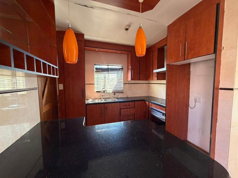 A functional kitchen featuring dark wood cabinetry, black granite countertops, a double sink, and built-in oven space.