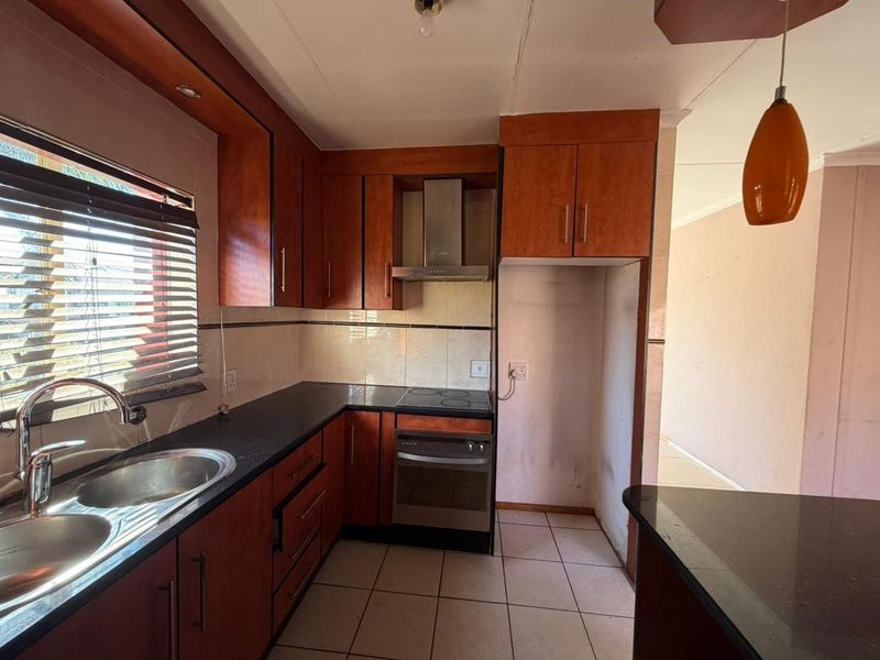 Functional kitchen featuring dark granite countertops, wood-veneer cabinetry, built-in electric oven and hob, stainless steel extractor fan, and double basin sink.