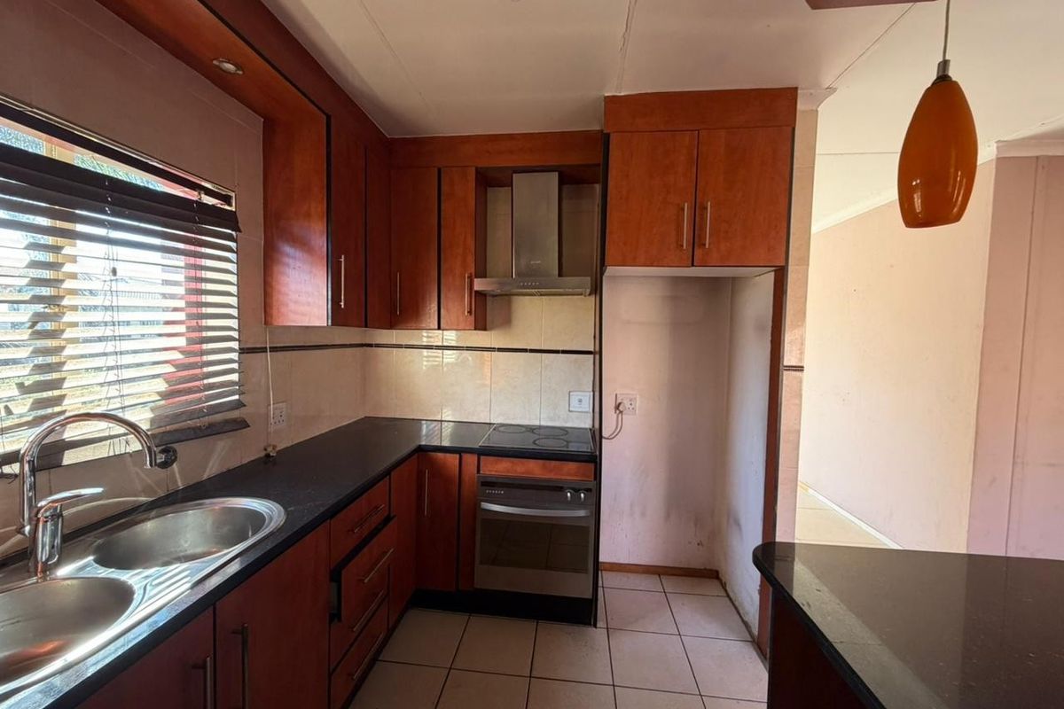 Functional kitchen featuring dark granite countertops, wood-veneer cabinetry, built-in electric oven and hob, stainless steel extractor fan, and double basin sink.