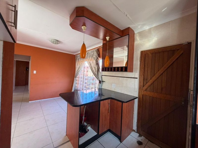 A kitchen area featuring a built-in breakfast bar with granite countertop, wooden cabinetry, and tiled flooring, leading into an adjacent living space.