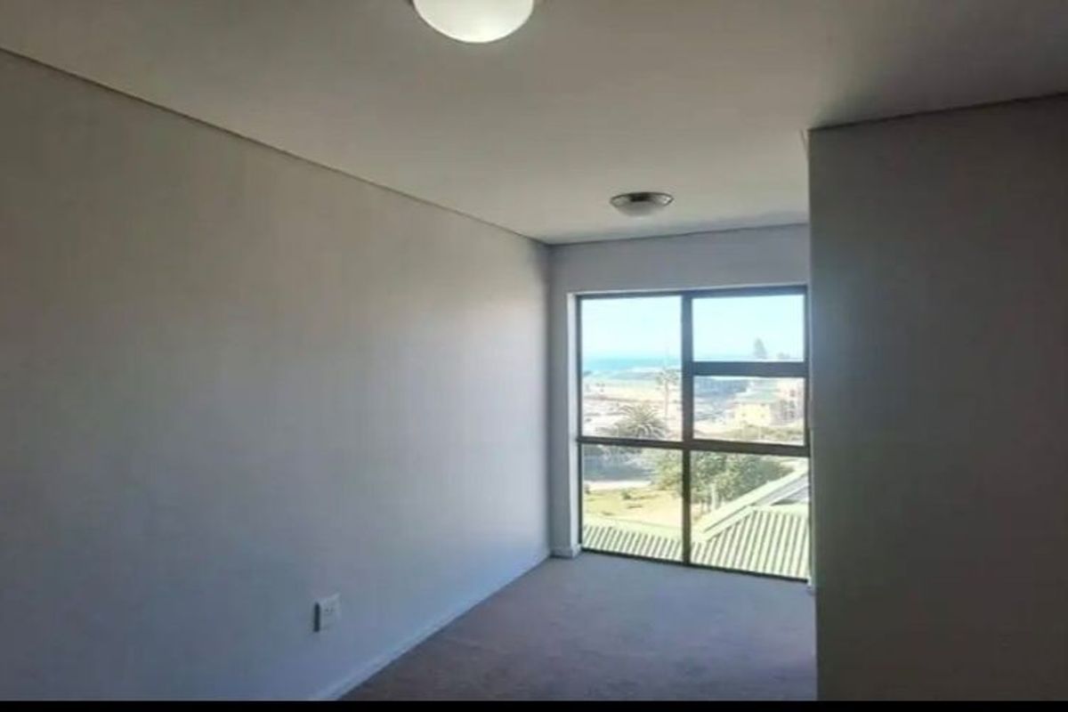 A bright, empty bedroom featuring neutral wall finishes, carpeted flooring, and a large window offering a view of the surrounding area.