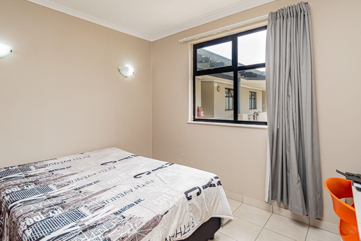 A functional bedroom featuring tiled flooring, wall-mounted lighting, and an aluminium-framed window with curtain tracks.