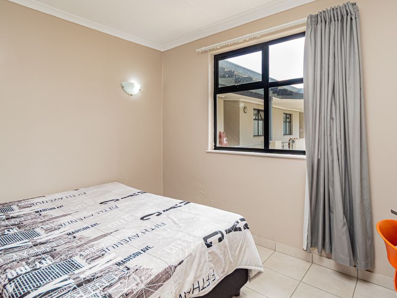 A functional bedroom featuring tiled flooring, wall-mounted lighting, and an aluminium-framed window with curtain tracks.
