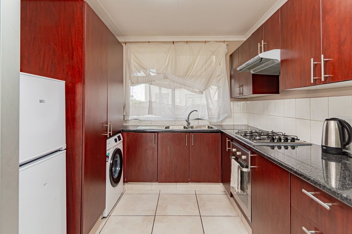 A functional galley-style kitchen featuring dark wood cabinetry, granite countertops, a gas hob, built-in oven, and integrated laundry plumbing.