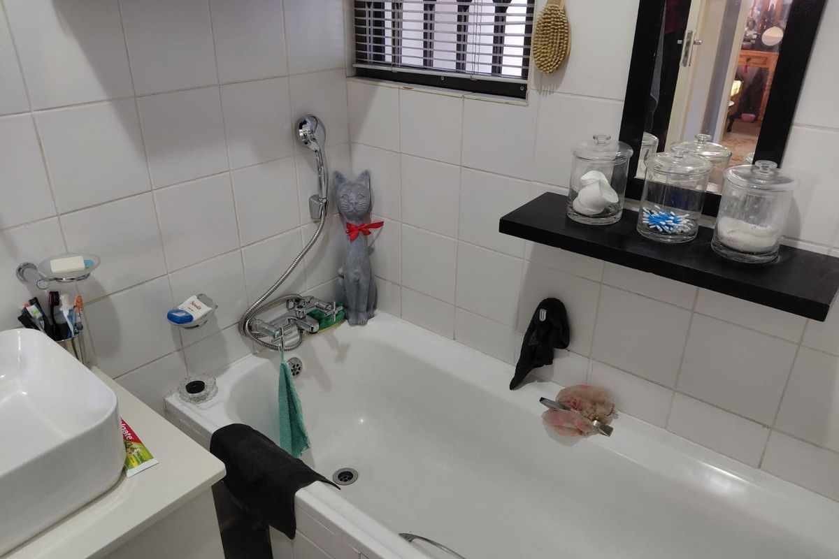 A functional bathroom featuring a white bathtub with a handheld shower mixer, a vanity basin, and wall-mounted shelving.